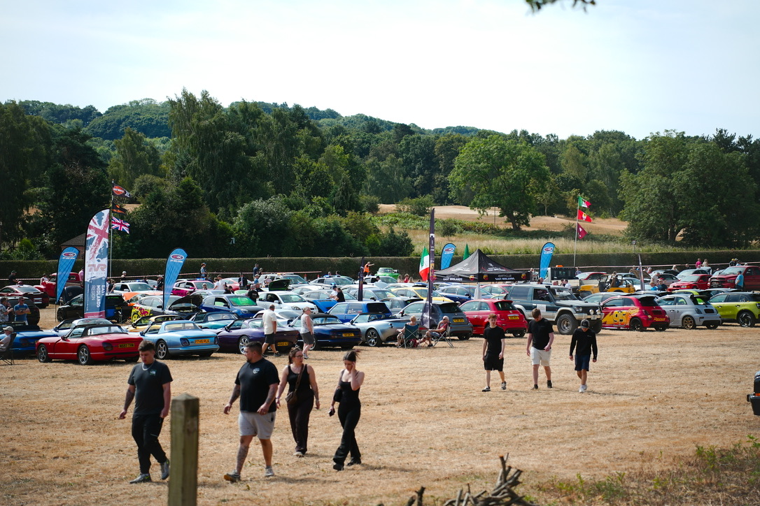 Crowd and cars across the field, club flags flying